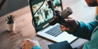 A man host streaming his audio podcast using microphone and laptop at his small broadcast studio, close-up