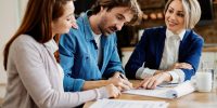 Young couple signing lease agreement while having meeting with real estate agent. Focus is on man.