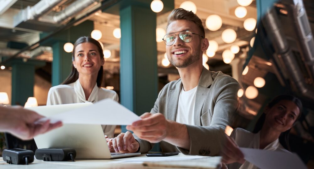 Beautiful young lady and handsome young man looking glad while receiving some documents from their manager