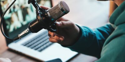 A man host streaming his audio podcast using microphone and laptop at his small broadcast studio, close-up