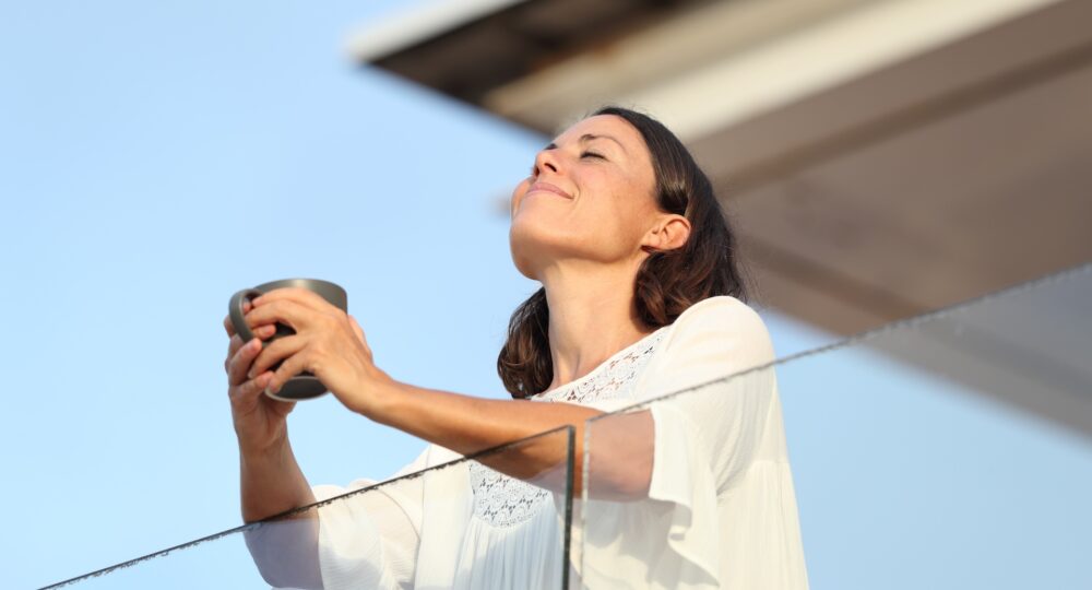 Adult woman with coffee cup breathing on a balcony